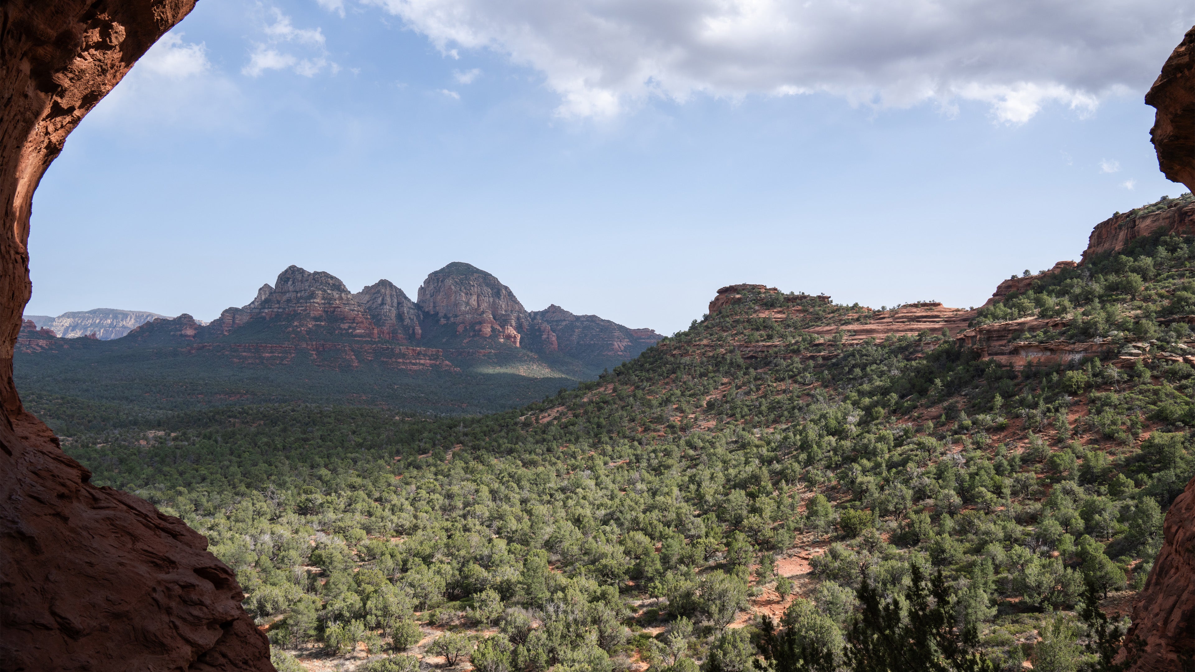 Scenic view of red rock formations and greenery from inside a cave.